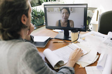 Male architect on video call with female coworker through computer at home office - MASF43355