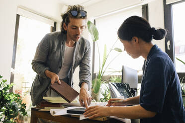 Male and female architects deciding on wooden plank at home office - MASF43358