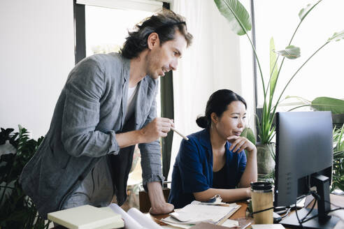 Male architect discussing with female colleague using computer at home office - MASF43360