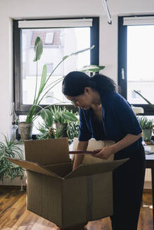 Mature female architect with plank and cardboard box at home office - MASF43368