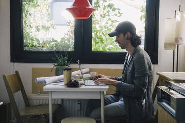 Side view of male architect using laptop at desk in home office - MASF43371