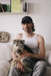 Portrait of man with dog sitting on sofa at home - MASF43388