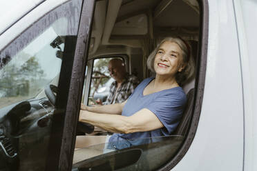 Smiling senior woman driving motor home with man during road trip - MASF43400
