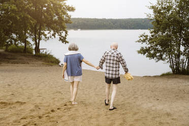 Full length of senior couple holding hands while walking towards river - MASF43415