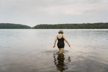 Rear view of senior woman walking in knee deep river - MASF43418