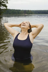 Happy senior woman with head in hands against river - MASF43422