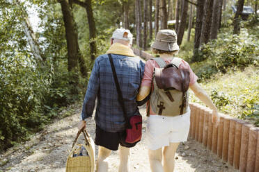 Rear view of retired senior couple walking together while hiking in forest - MASF43426