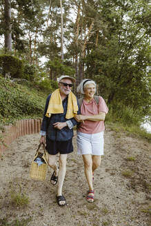 Full length of smiling retired senior couple walking together while hiking in forest - MASF43430