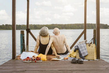 Rear view of senior couple sitting on gazebo while looking at river against sky - MASF43435