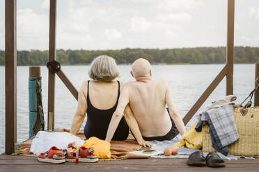 Senior couple sitting on gazebo while looking at river against sky - MASF43436