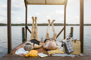 Full length of senior couple lying with legs up on gazebo over river - MASF43439