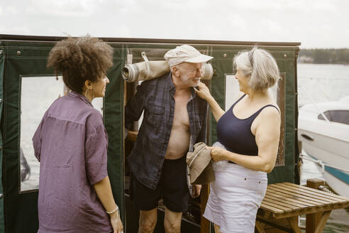 Smiling senior couple near young woman standing on houseboat - MASF43443