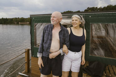 Happy senior couple standing with arm in arm on houseboat - MASF43444