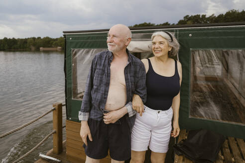 Happy senior couple standing with arm in arm on houseboat - MASF43444