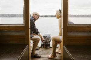 Happy senior couple talking while sitting at houseboat - MASF43445