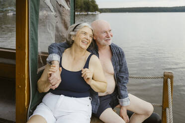 Happy senior couple sitting with arm around on houseboat - MASF43448