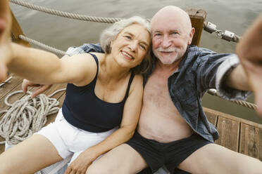 Happy senior couple taking selfie while sitting on houseboat - MASF43449