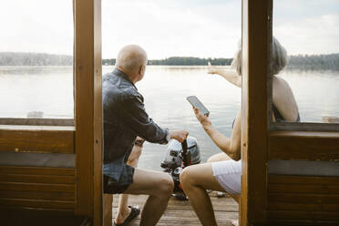 Senior couple with smart phone sitting on houseboat - MASF43451