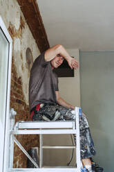 Smiling male worker sitting on ladder in break at site - MASF43462