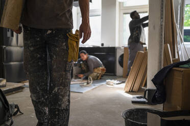 Midsection of carpenter carrying plank while coworkers working in kitchen at home - MASF43467