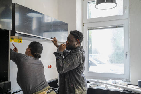 Diverse male and female carpenters working together in kitchen at apartment - MASF43475