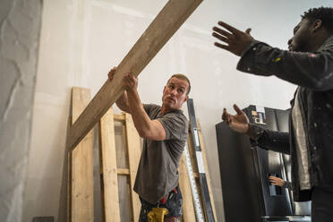 Multiracial male carpenters carrying plank while working in apartment - MASF43482