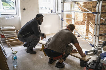 Multiracial male carpenters crouching in front of plank while in apartment - MASF43484