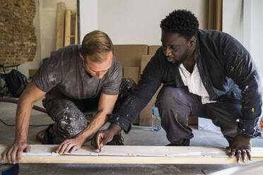 Diverse male carpenters marking with pencil on plank while working in apartment - MASF43485