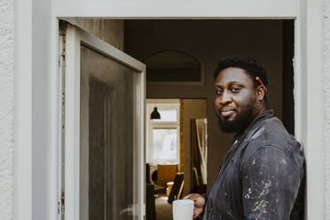 Side view portrait male carpenter holding coffee cup at doorway of house - MASF43513