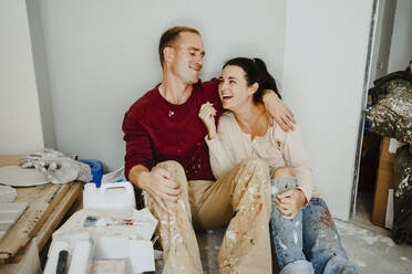 Cheerful couple sitting together in room while renovating home - MASF43521