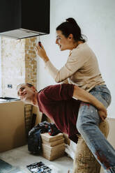 Man piggybacking woman fixing lighting equipment while renovating home together - MASF43523
