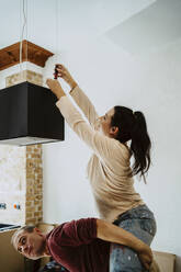 Happy couple fixing lighting equipment while renovating home - MASF43524