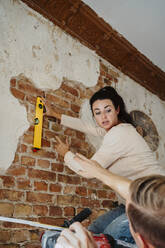 Man assisting woman in measuring brick wall while renovating home - MASF43528