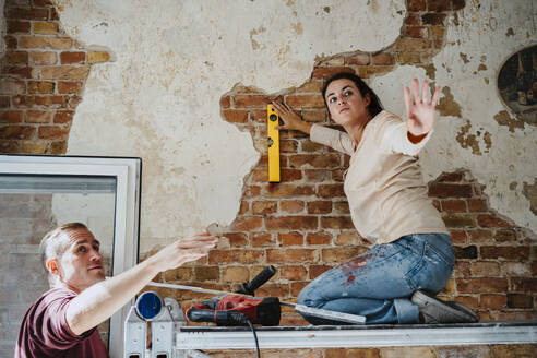 Couple discussing while measuring brick wall during home renovation - MASF43530