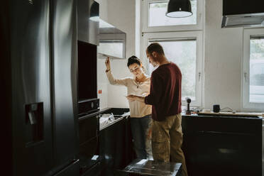 Couple discussing while fixing cabinet in kitchen during home renovation - MASF43533