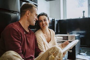 Happy couple discussing over wood in kitchen while renovating home - MASF43538