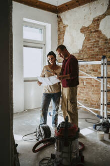 Couple discussing over blueprint in room while renovating home - MASF43544