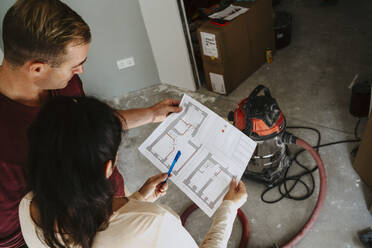 High angle view of couple discussing over blueprint while renovating home - MASF43547