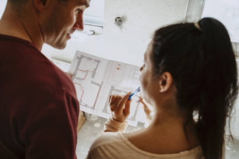 High angle view of couple discussing over blueprint while renovating home - MASF43549