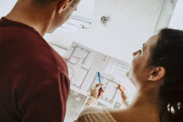 Rear view of couple discussing over floor plan while renovating home - MASF43550