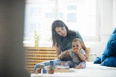 Mother with playful baby girl sitting on bed at home - JOSEF23834