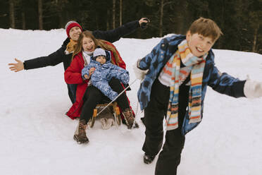 Glücklicher Junge, der seine Familie auf einem Schlitten durch den Winterwald zieht - MCHF00006
