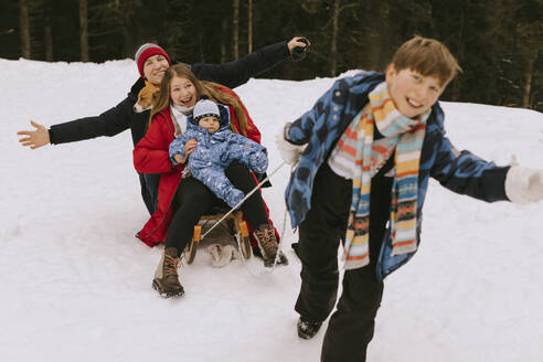 Happy boy pulling family on sled in winter forest - MCHF00006