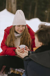 Lächelnde Frau hält Teetasse mit Freund im Winter - MCHF00010