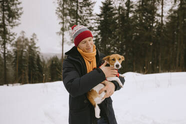 Lächelnder Mann hält seinen Hund im Winterwald - MCHF00016
