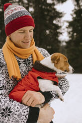 Man and dog wearing warm clothes in winter forest - MCHF00018
