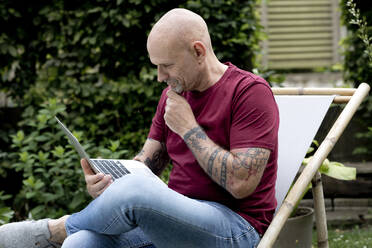 Mature freelancer with hand on chin using laptop in garden - FLLF00905