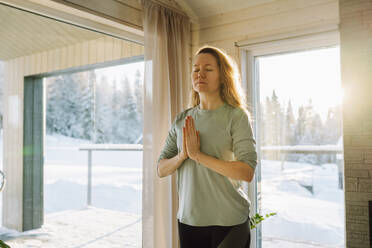 Woman with eyes closed standing in prayer yoga pose at home - OLRF00207