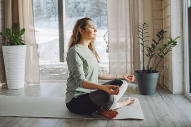 Frau sitzt in Lotus-Yoga-Pose zu Hause - OLRF00209