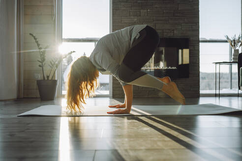 Woman doing crane yoga pose on exercise mat at home - OLRF00213